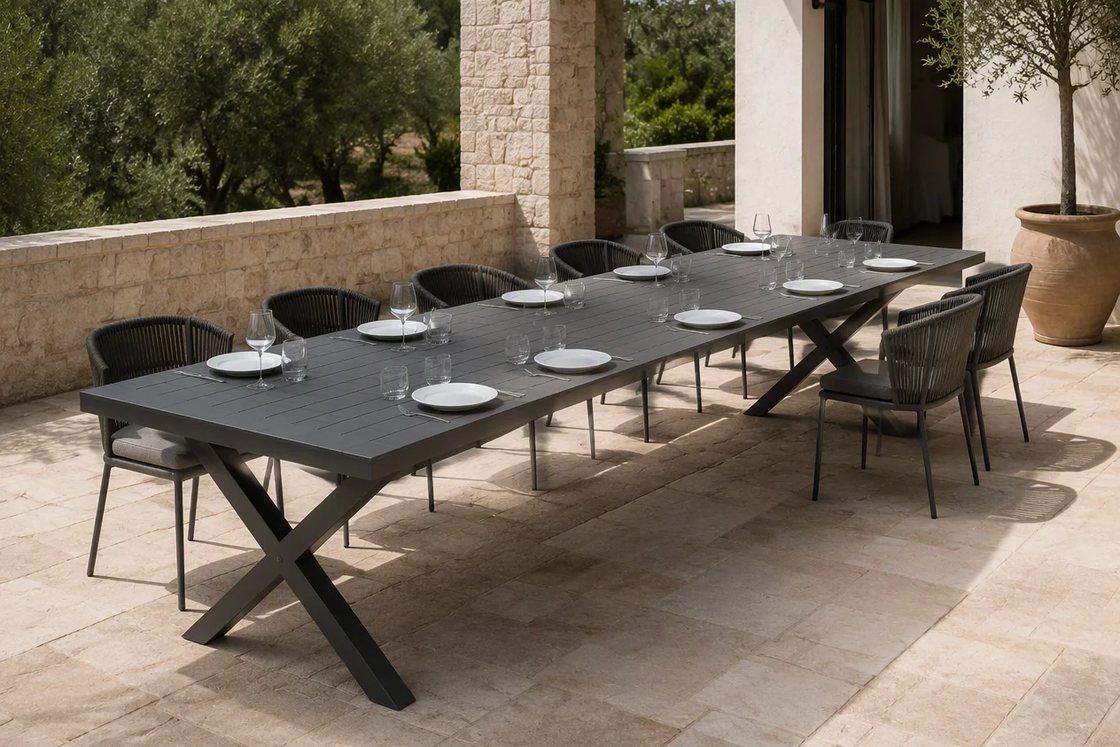 An aluminium slat outdoor dining table set for ten at its extended length, on a stone terrace