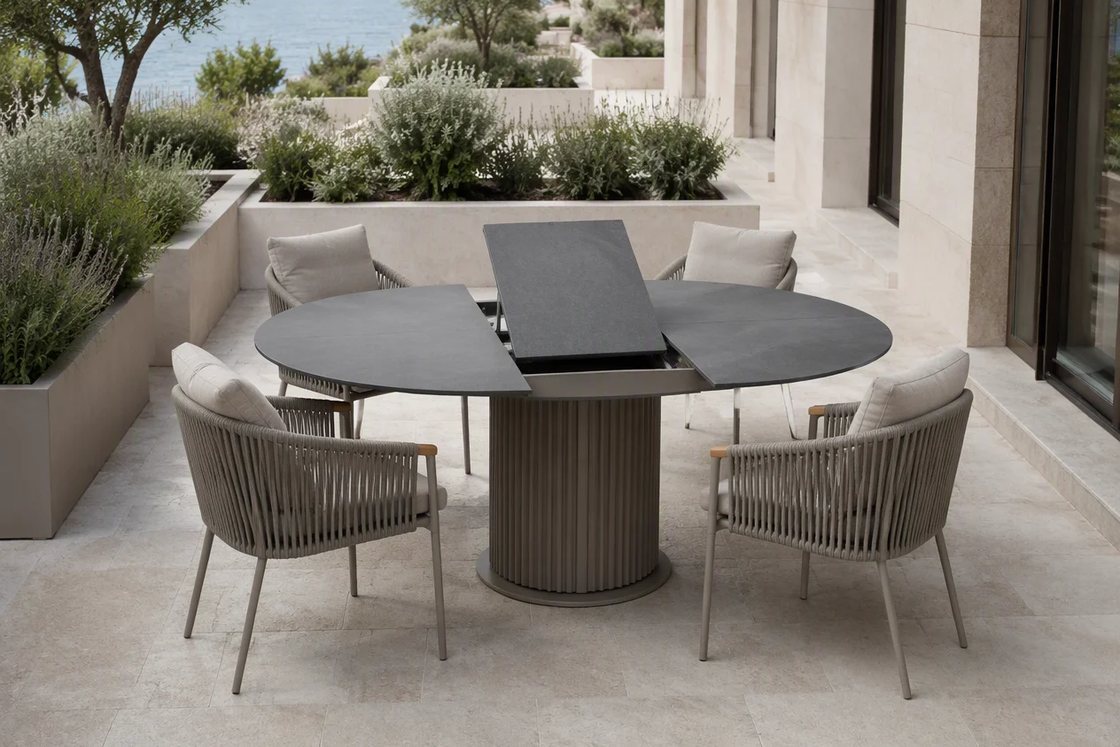 A round outdoor dining table with its centre panel raised, set with rope weave chairs