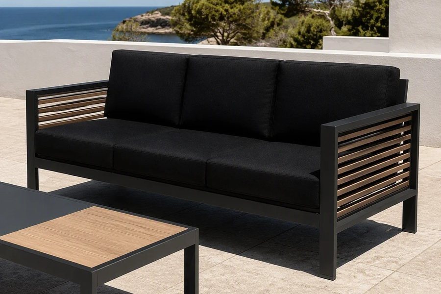 A charcoal outdoor lounge sofa with light wood-look slat panels across the arms, with a wood-top table in front
