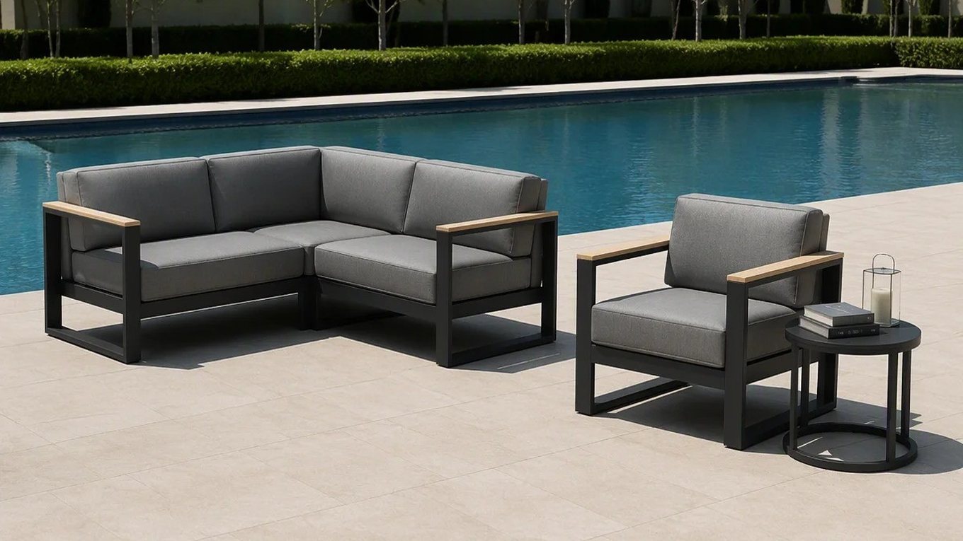 A corner module, a single armchair and a round side table in a charcoal outdoor lounge set, beside a pool