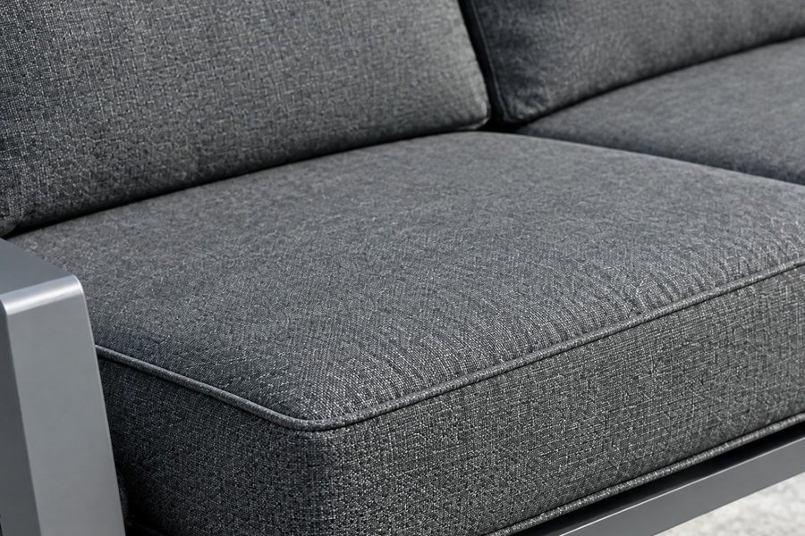 A thick grey outdoor seat cushion with a piped edge on a dark aluminium sofa frame