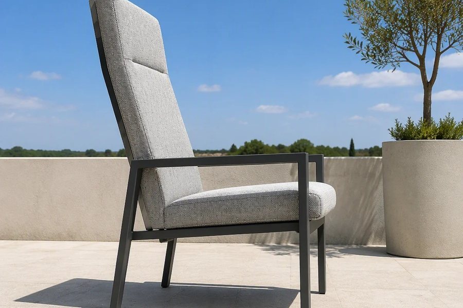 The same light grey high-back outdoor armchair from a lower front angle, with a planter beside it