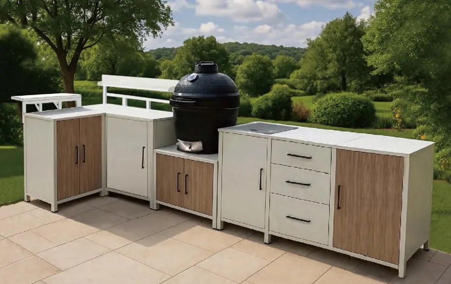 The white and tan outdoor kitchen installed on a paved patio with a kamado grill, lawn and trees behind