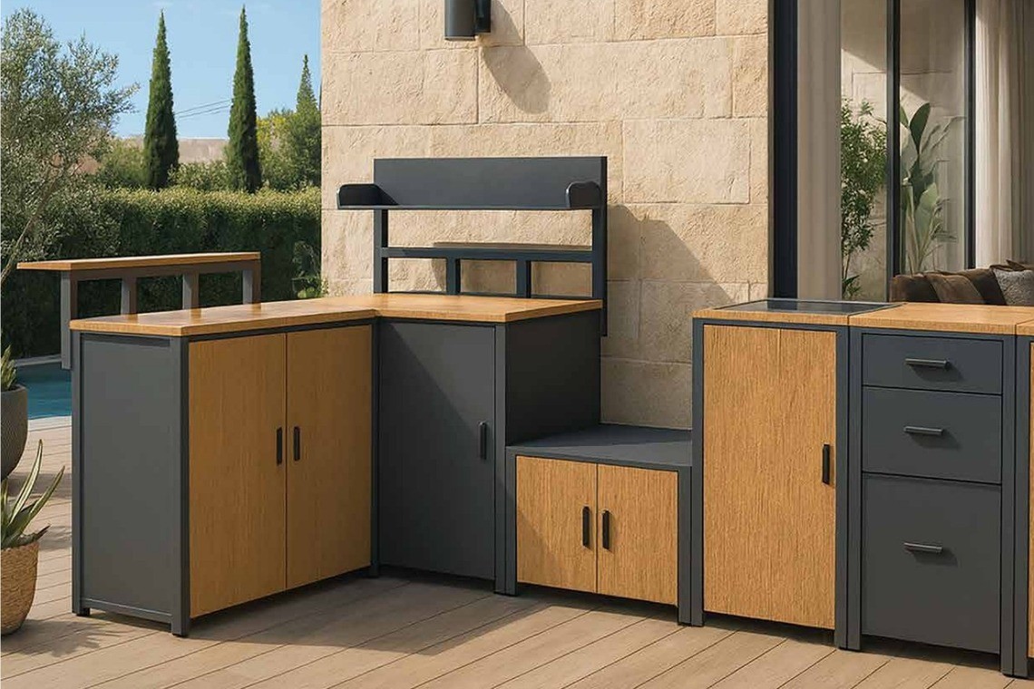 A dark grey and teak modular outdoor kitchen with rock plate countertops on a timber deck beside a pool, against a stone wall
