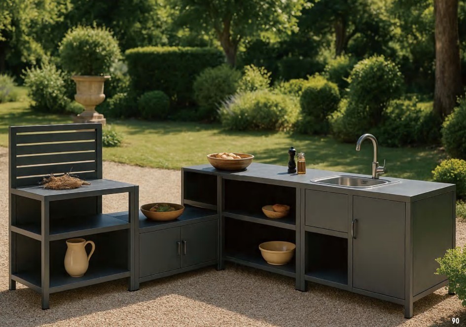 Outdoor kitchen run with a storage table, an oven table, cabinets and a sink table on gravel in a clipped garden