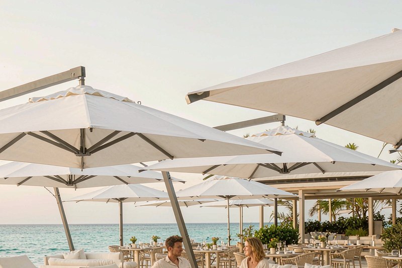 Beach resort pool deck with white cantilever umbrellas over loungers facing the sea