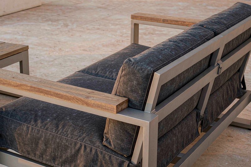 Close-up of an aluminium lounge frame with a teak armrest and grey cushions