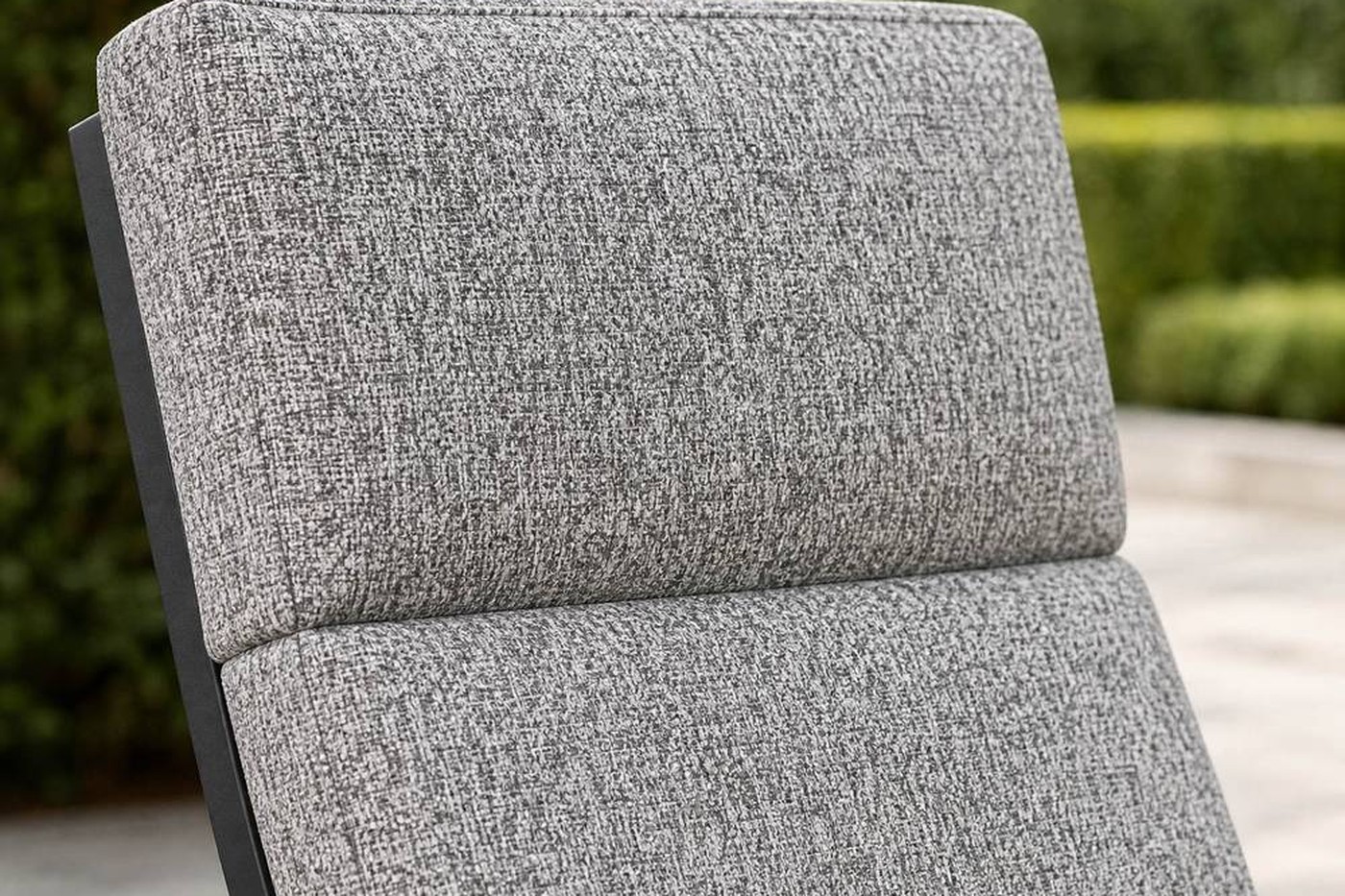 Close-up of a mid grey speckled outdoor seat cushion with a rounded front edge and simple seams on a charcoal aluminium armchair