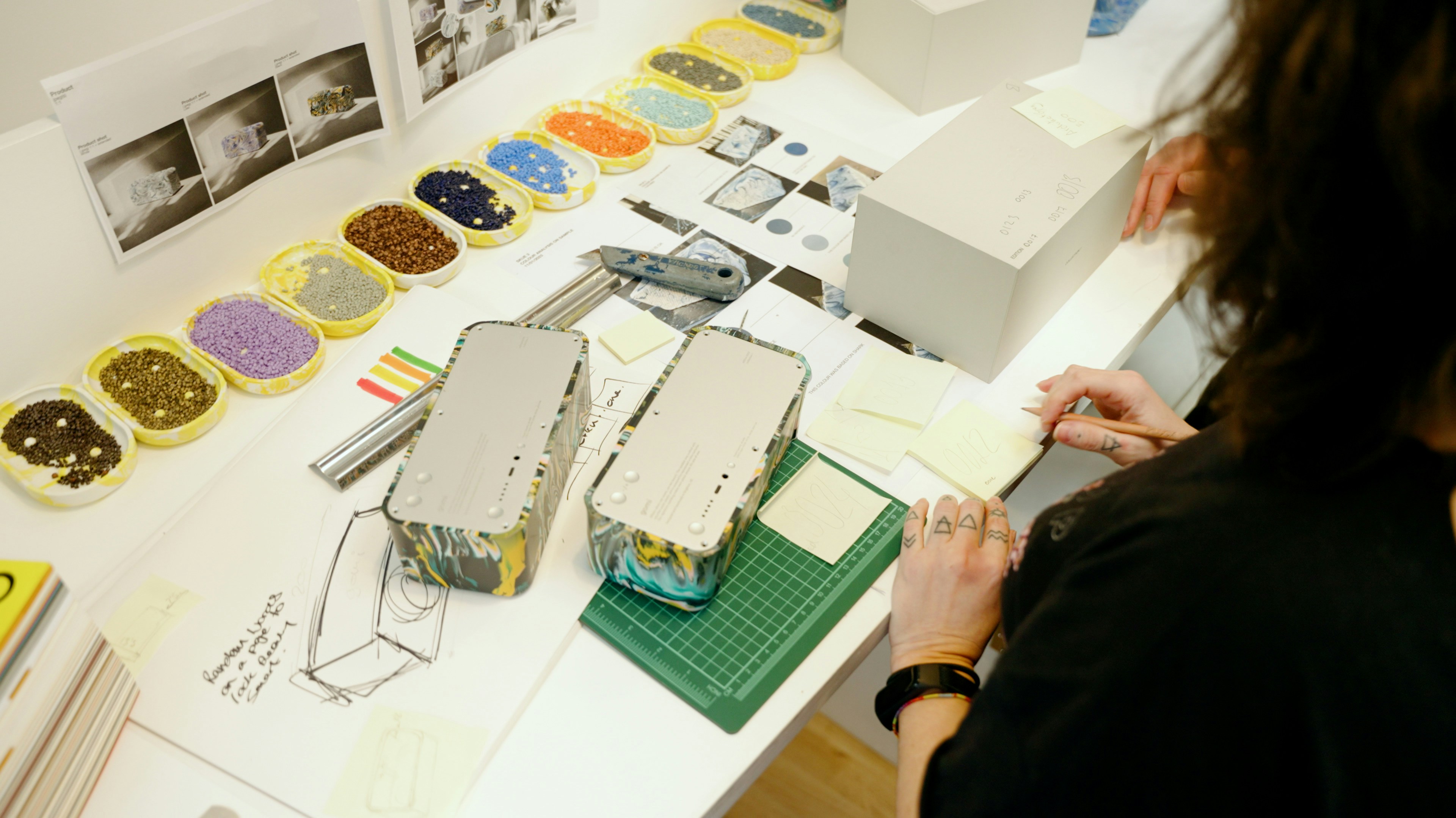 A designer carefully inspecting a sample hoodie against a tech pack on a table.