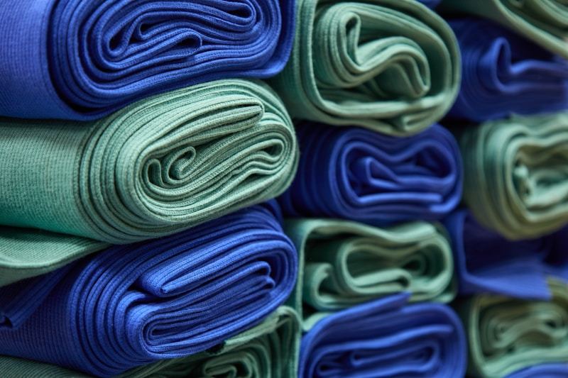 Stacked colorful fabric rolls in blue and green tones for sustainable clothing production