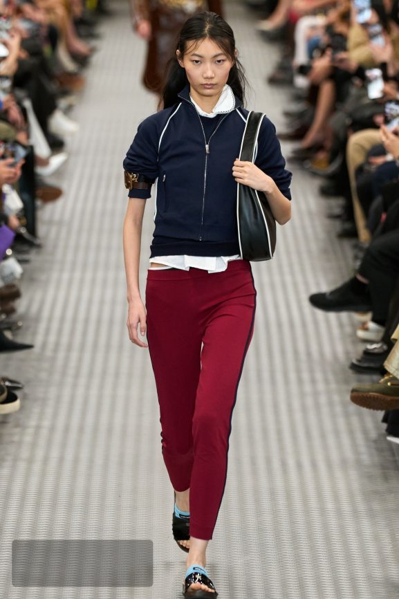 Miu Miu runway look combining a navy technical jacket and red trousers — the brand’s signature tension between schoolgirl and athlete