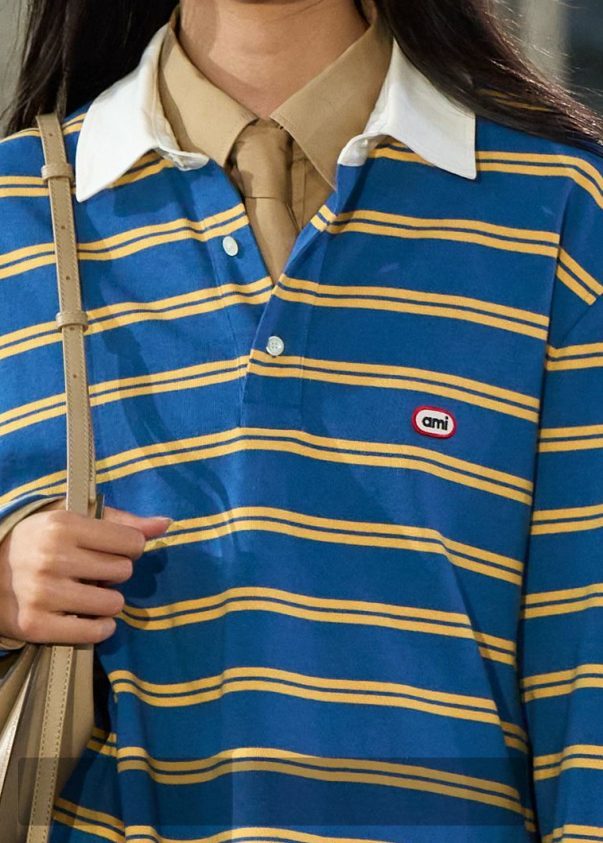 A blue striped rugby polo layered under a sweater — the FW26 reference for Après-style contrast layering