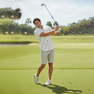 Golfer mid-swing wearing golf cart print short sleeve polo on sunny fairway