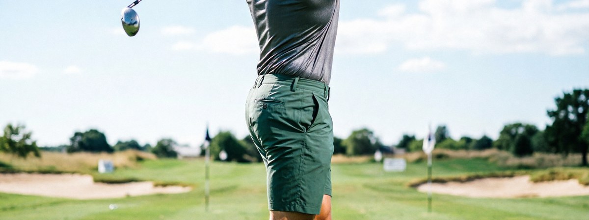 Caucasian European male golfer demonstrating a full rotational swing in a moisture-wicking four-way-stretch golf polo on a practice range