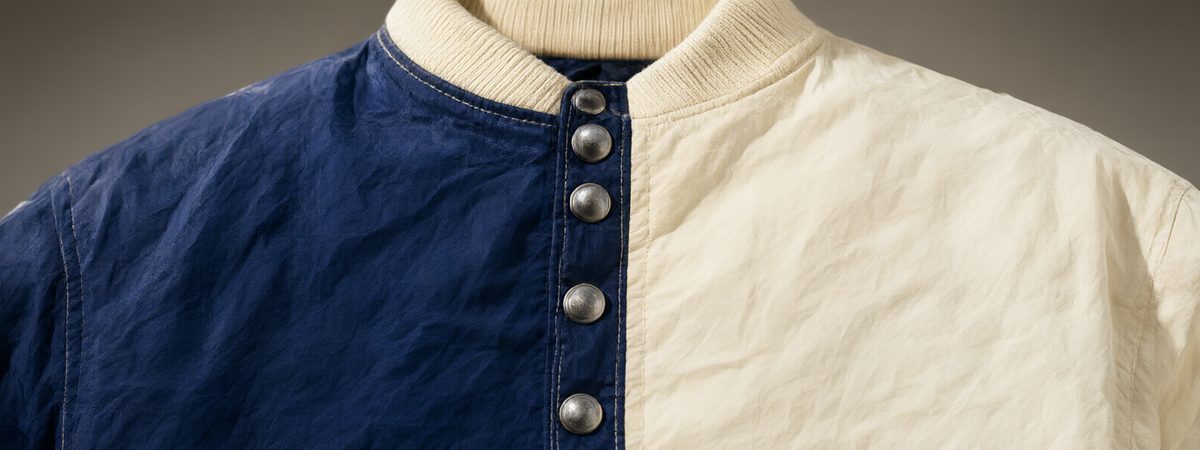 Close-up of a vintage warm-up jacket snap-front placket with metal snap buttons, stand collar and ribbed trim in cream and navy color-block