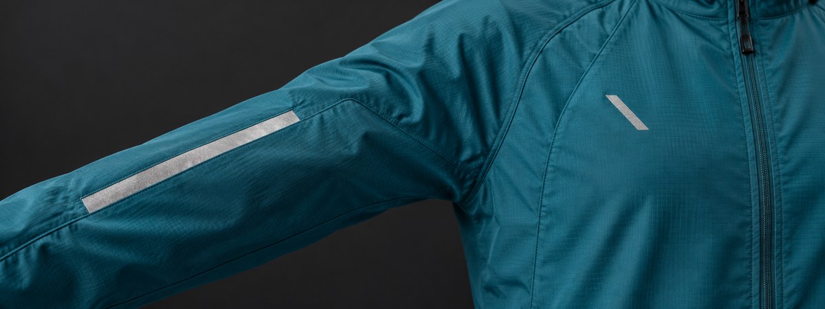 Silver reflective placement accents on a teal running jacket sleeve and chest