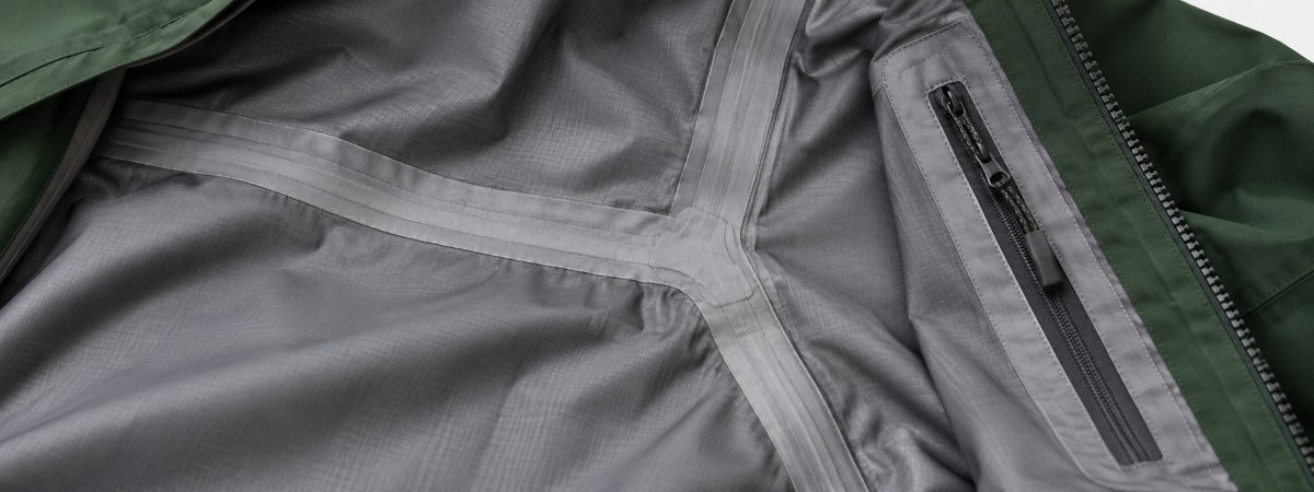 Gray hardshell interior with tape covering a seam junction beside a zipper backing