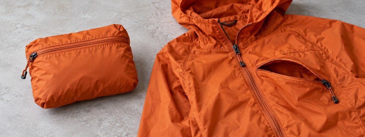 Orange lightweight shell demonstrating its compact pack-away pocket