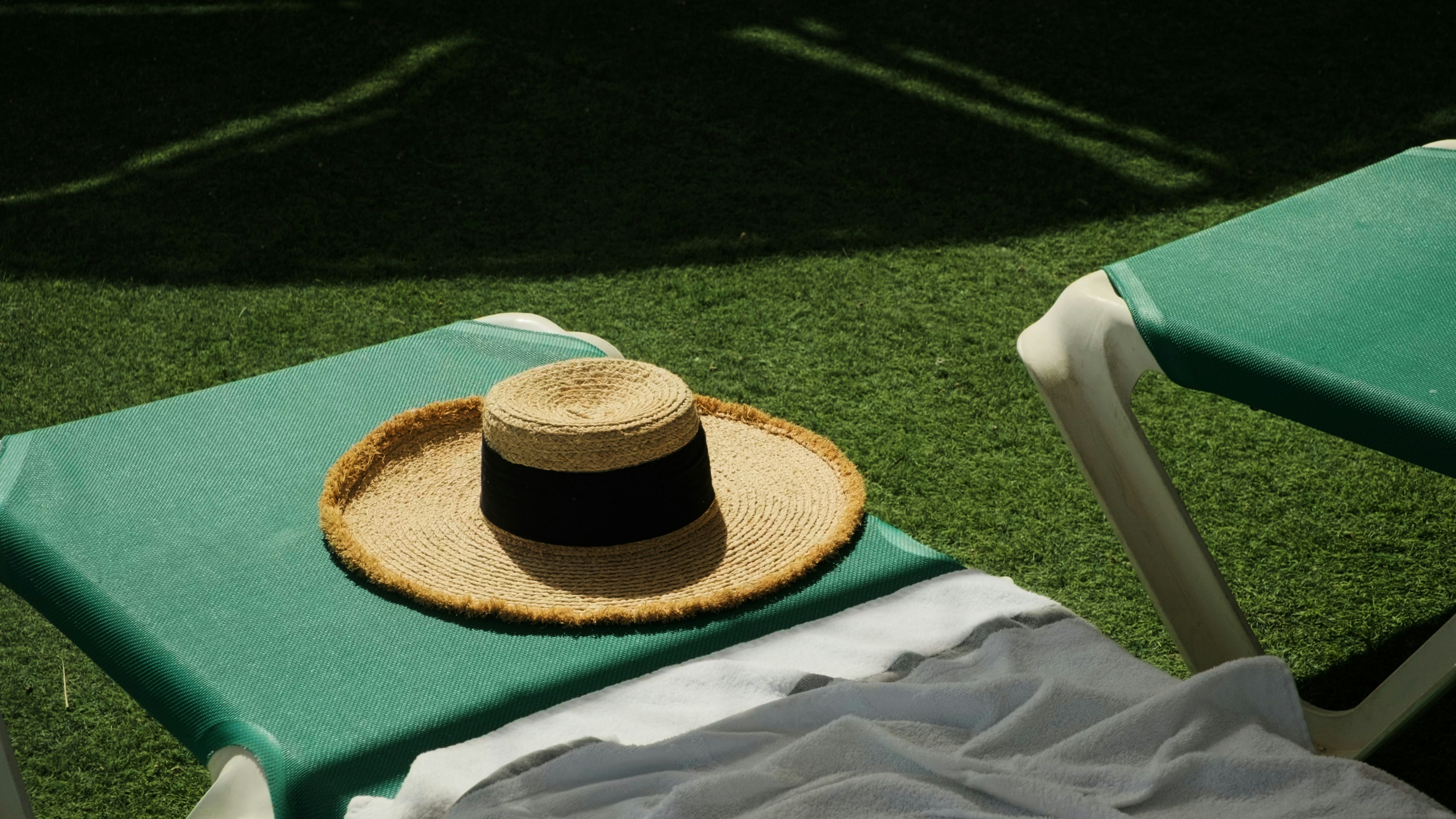A collection of poolside essentials including a sun hat, sunglasses, sunscreen, and a towel.