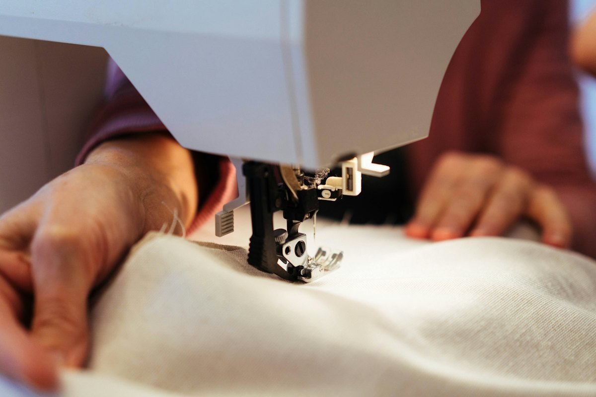 Hands guiding fabric through a sewing machine during garment construction