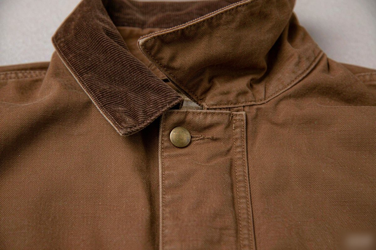 Close-up of a wide-wale contrast corduroy collar with edge binding, topstitching and a matte metal snap on a brown duck canvas barn jacket