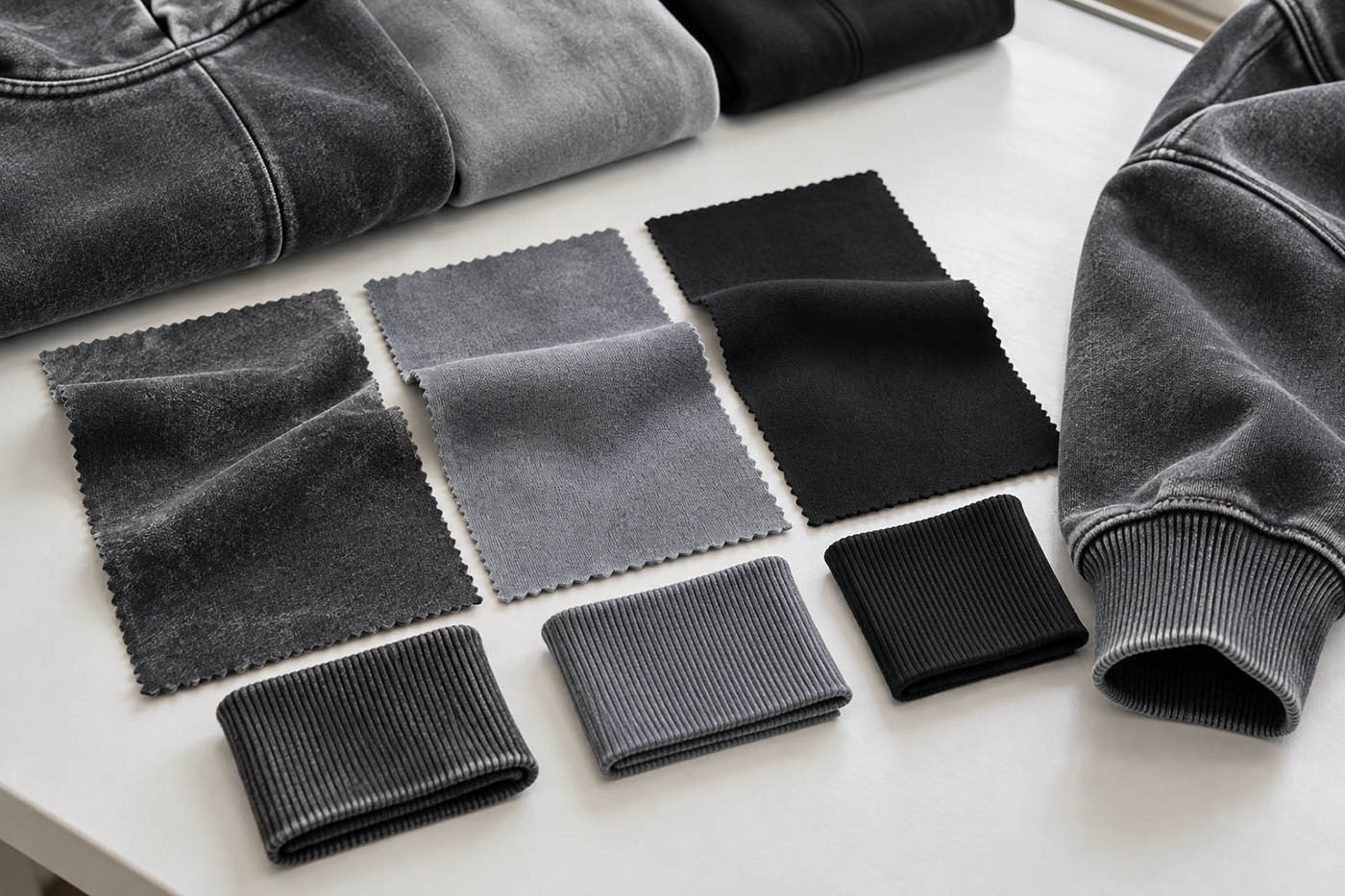 Textile swatches in washed charcoal, gray and deep black with visible hoodie fleece and rib details