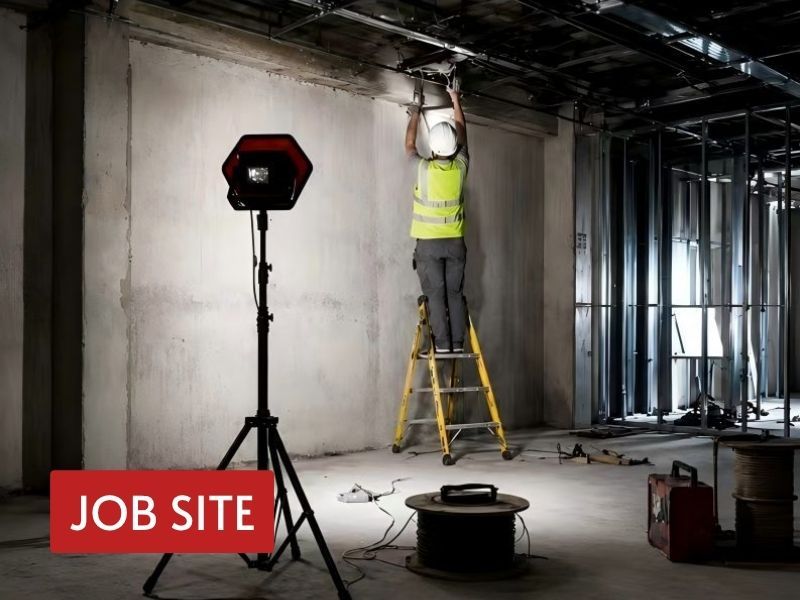 bright led flood light on a tripod illuminating an indoor construction jobsite for overhead installation work