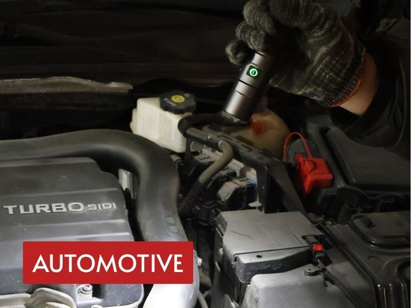 portable edc flashlight held by a mechanic to inspect hoses and electrical components inside a vehicle engine bay
