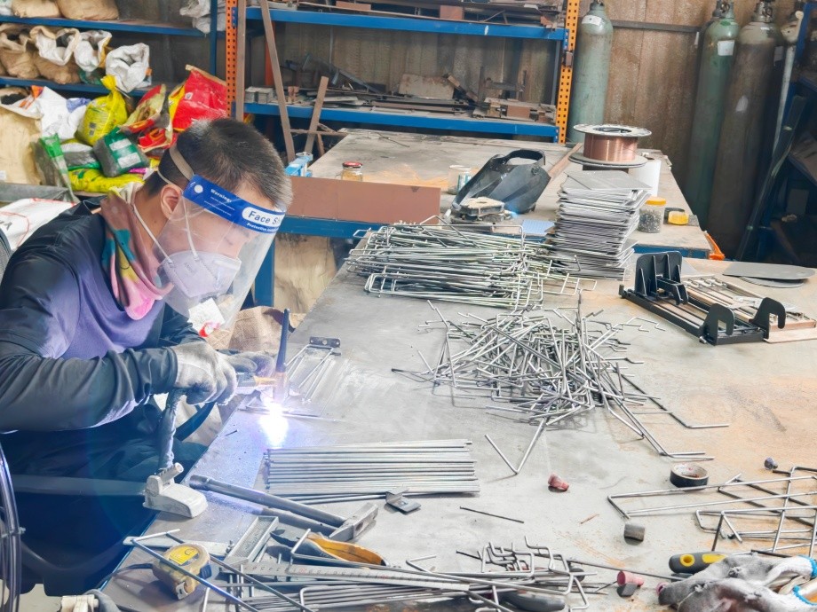 Welder joining steel tube frame sections of a retail display stand under protective equipment