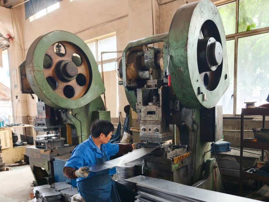 Sheet metal punching press operated by a technician, forming steel display frame components to a customer drawing