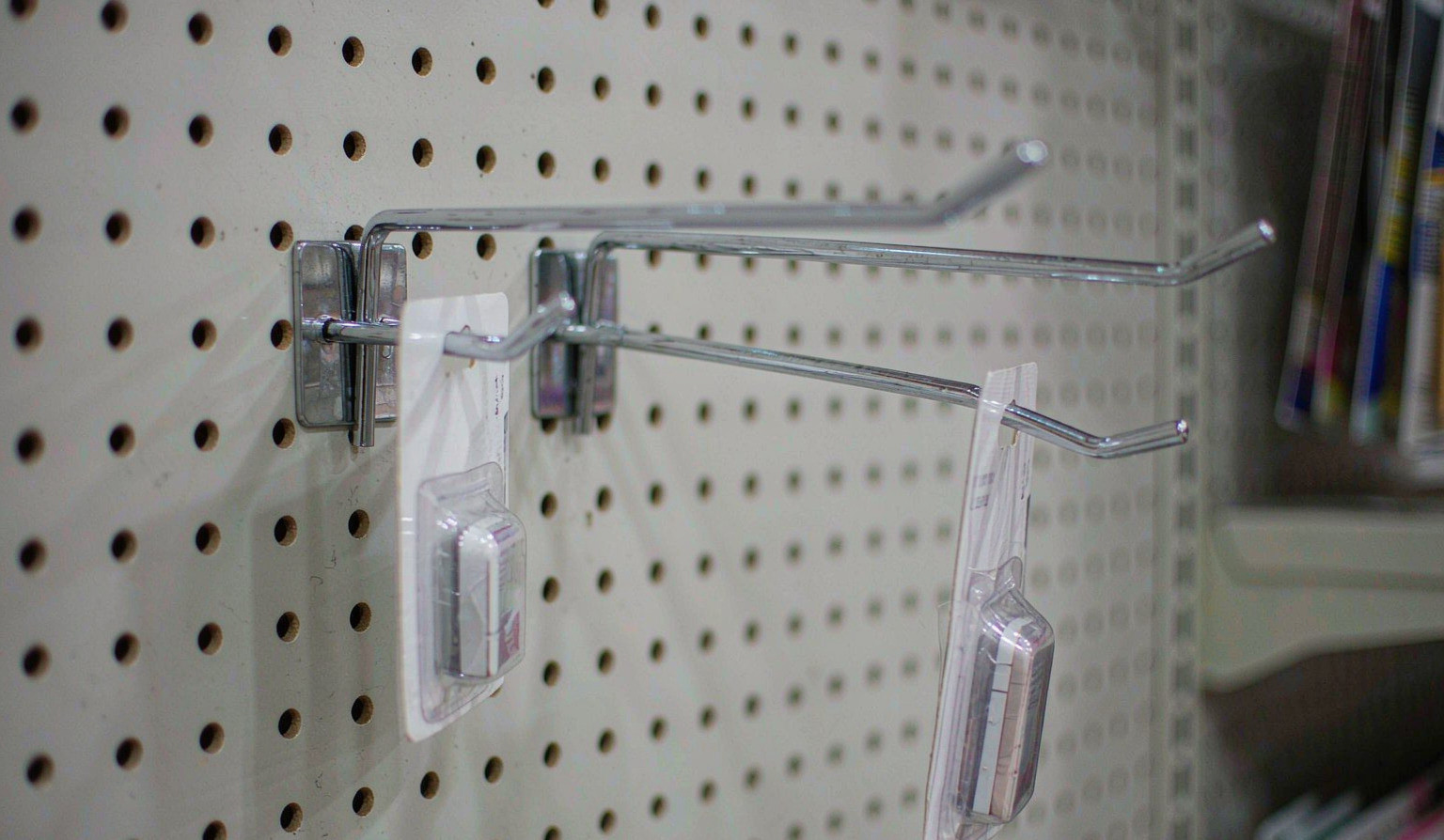 Chrome pegboard display hooks on a white perforated panel, packaged items hanging from the straight wire arms