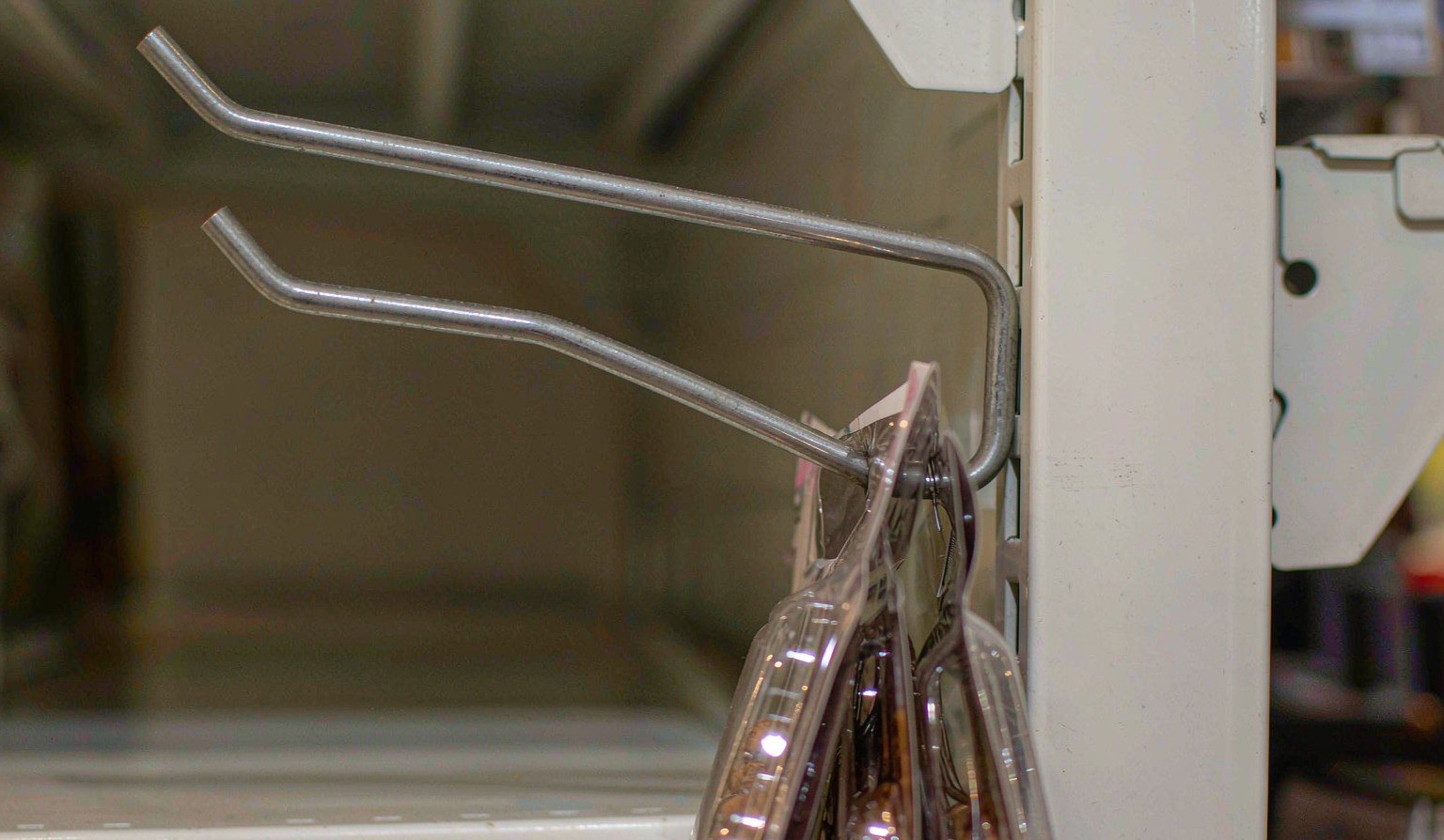 Close-up of a metal retail display hook on a slatwall panel with packaged products bunched against the base of the arm