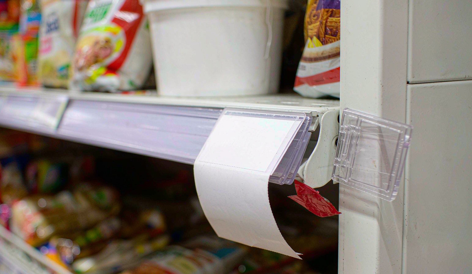 A white price card slipped out of its clear shelf-edge holder and hanging crooked