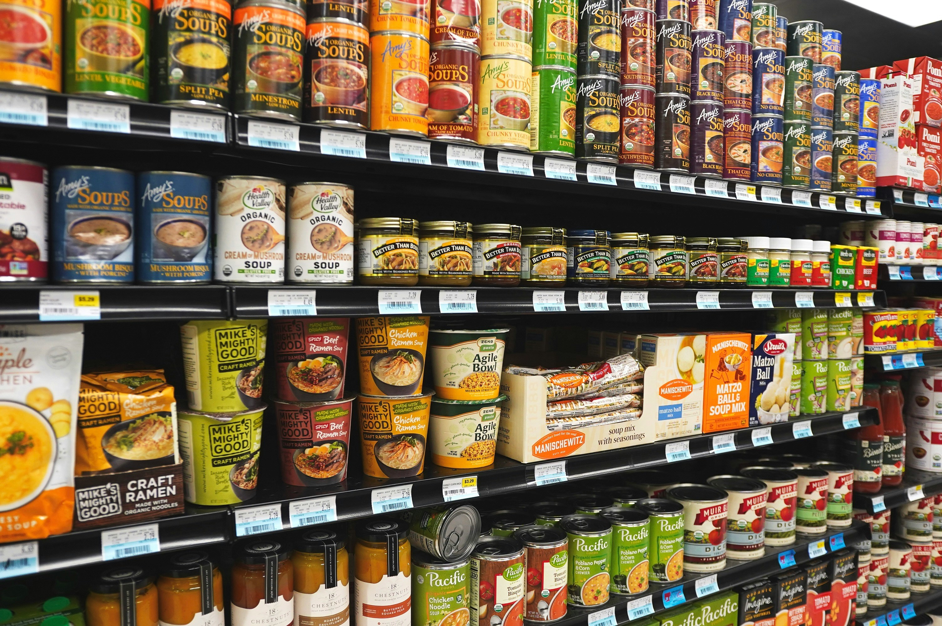 Supermarket shelf fronts running one above another, each carrying a continuous price strip with printed cards