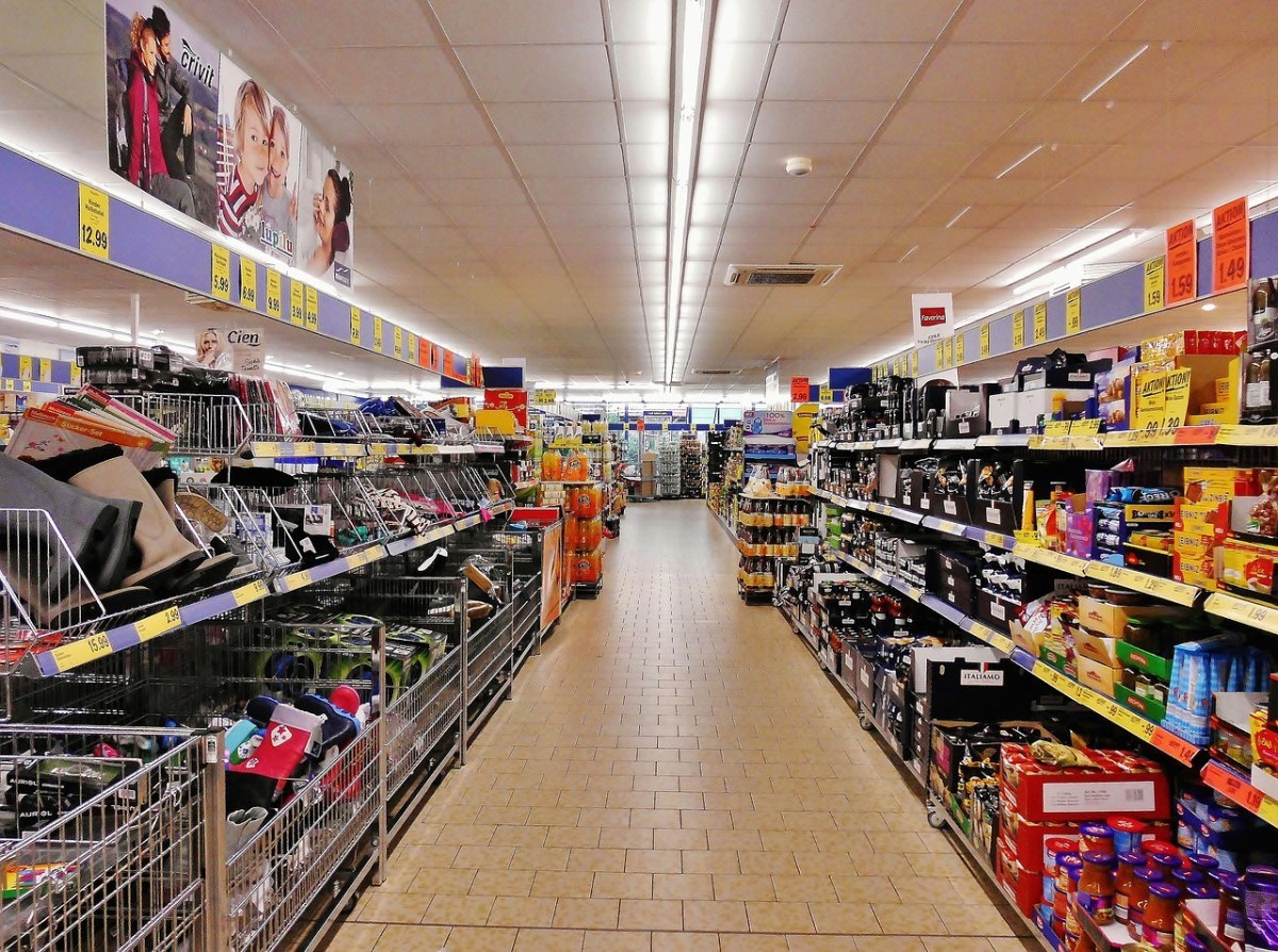 A store aisle with both shelf runs fully loaded and labelled along the front edge