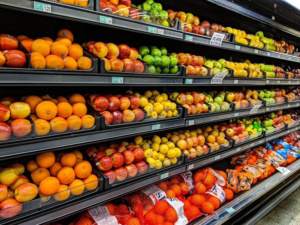 Supermarket produce display with crates of oranges, apples and lemons on sloped display shelves