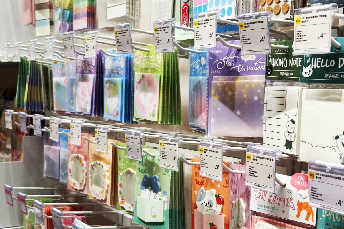 Rows of double-prong euro hooks holding envelopes, sticker packs and notebook refills in a stationery bay, each hook carrying a clear label holder