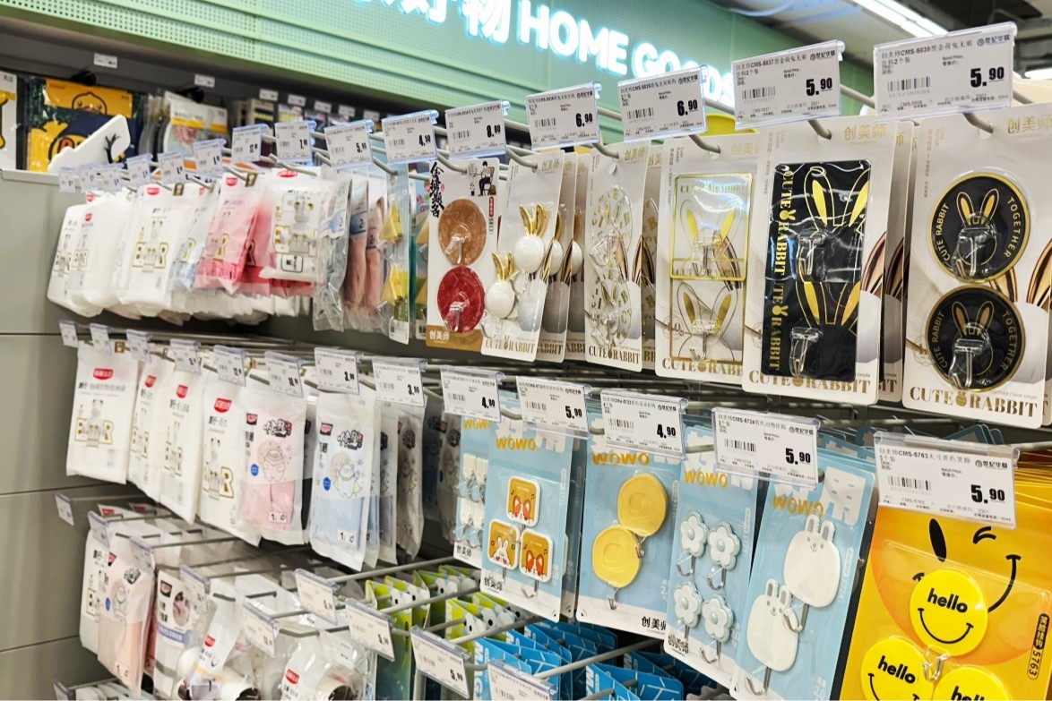Carded homeware and decorative hooks hanging from white double-wire hooks below an overhead price strip in a housewares aisle