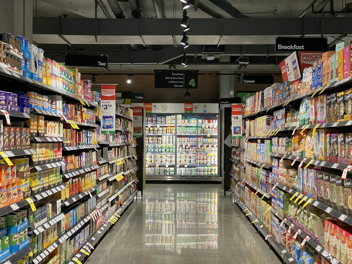 Supermarket drinks aisle with a glass door beverage cooler at the end, packed shelves on both sides