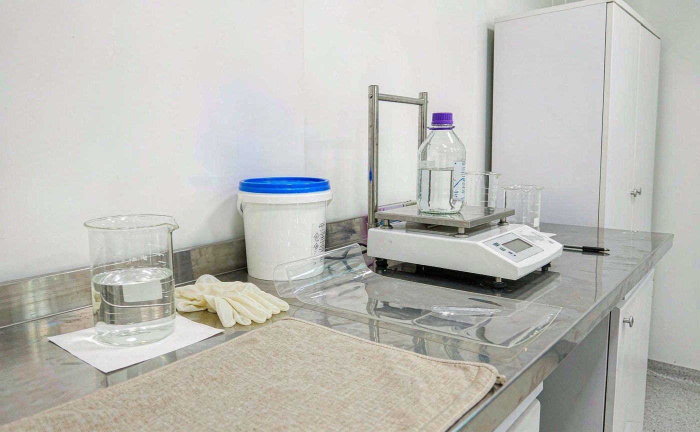 Transparent UV-curable resin sample and packaging bucket in a coatings laboratory