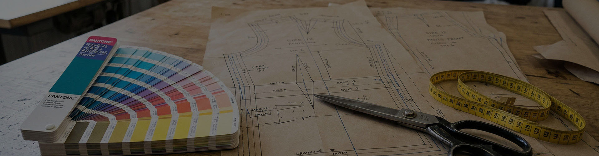 Professional activewear pattern making and sample development process, featuring a Pantone color guide, technical paper drafts, and tailoring tools for custom garment manufacturing.