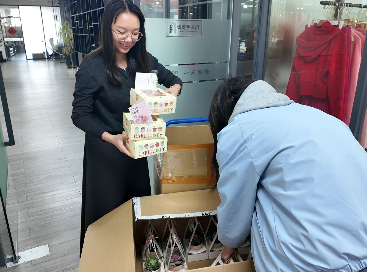 Call The STYLE staff distributing Women's Day gifts in our Dongguan activewear manufacturing office, with sample clothing racks in the background.