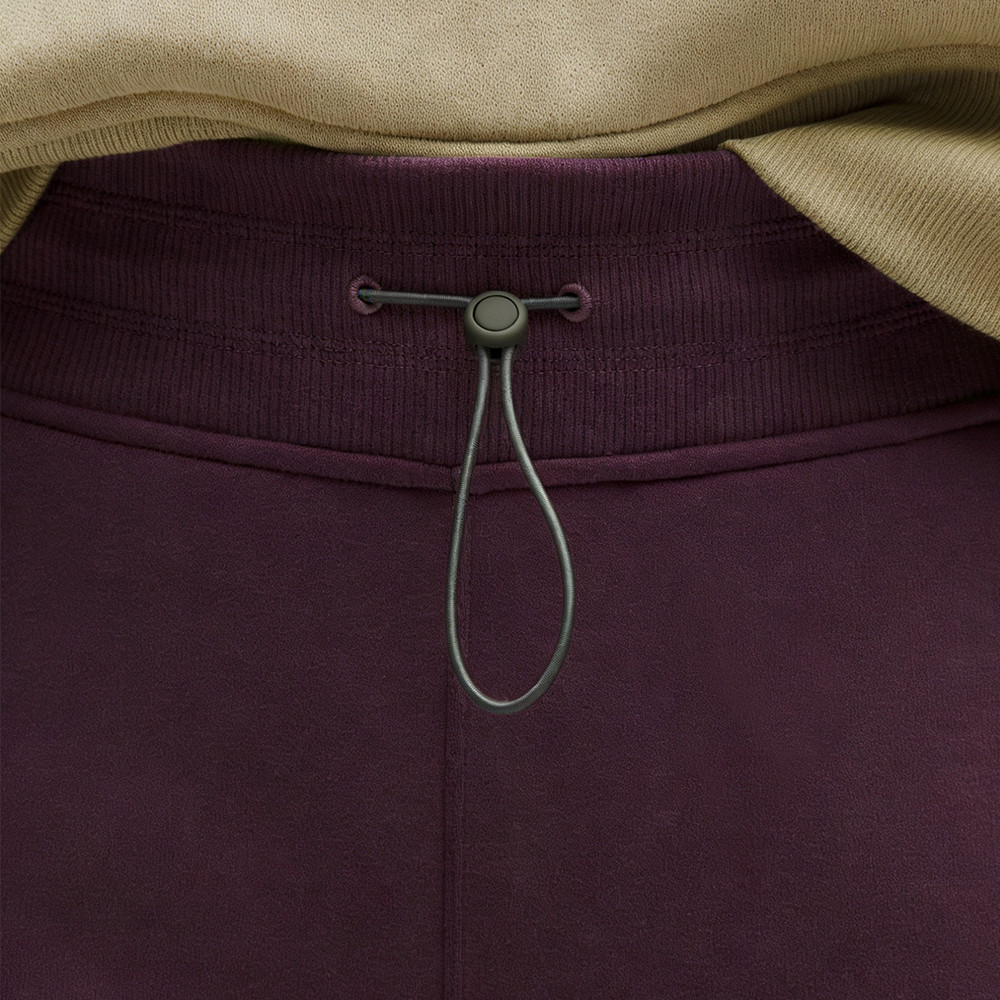 Close-up of the elastic waistband of dark purple wide-leg pants, featuring matching drawstring with matte metal eyelets and a visible front vertical pintuck seam.