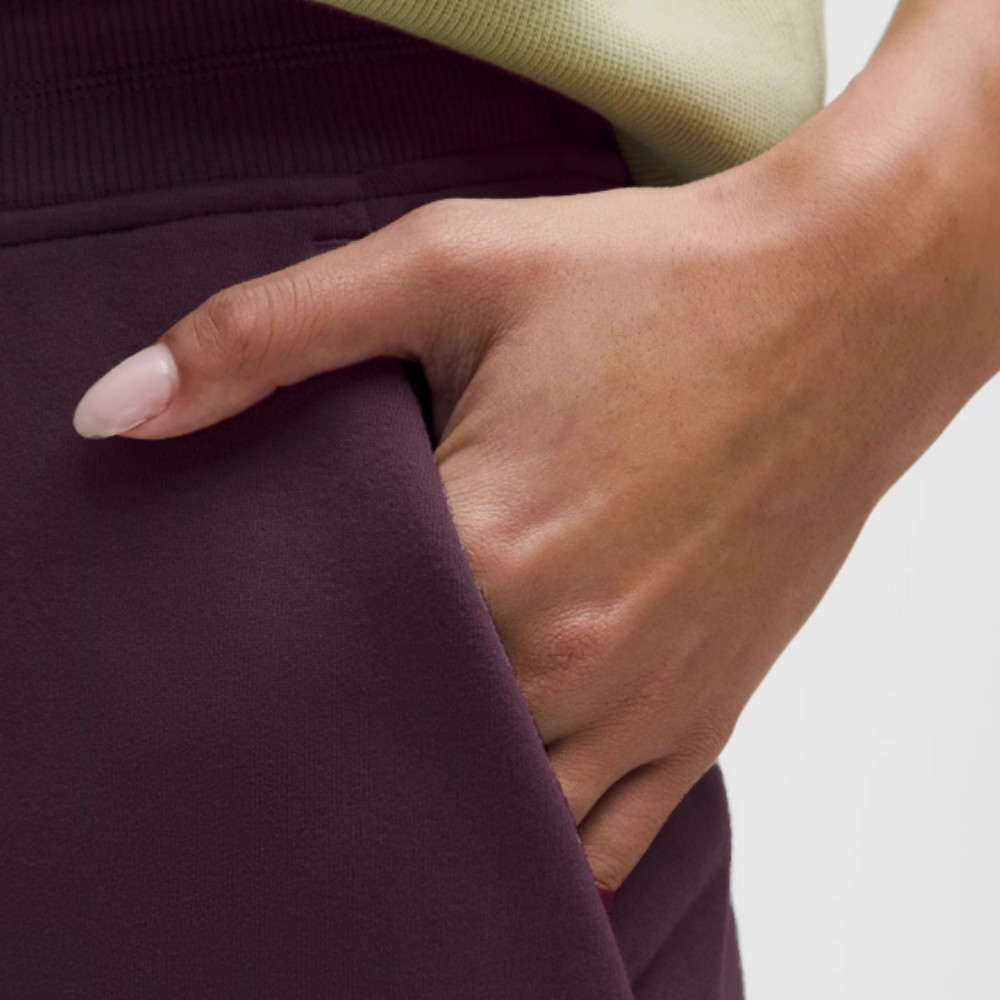 Close-up detail of the side pocket entry and the vertical front pintuck seam on dark purple wide-leg sweatpants.