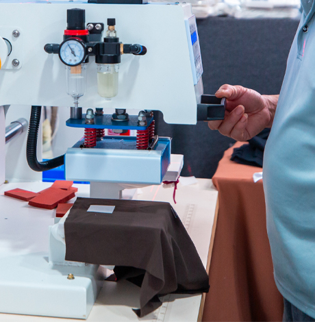 Worker operating heat transfer machine for custom branding and logo application on activewear.
