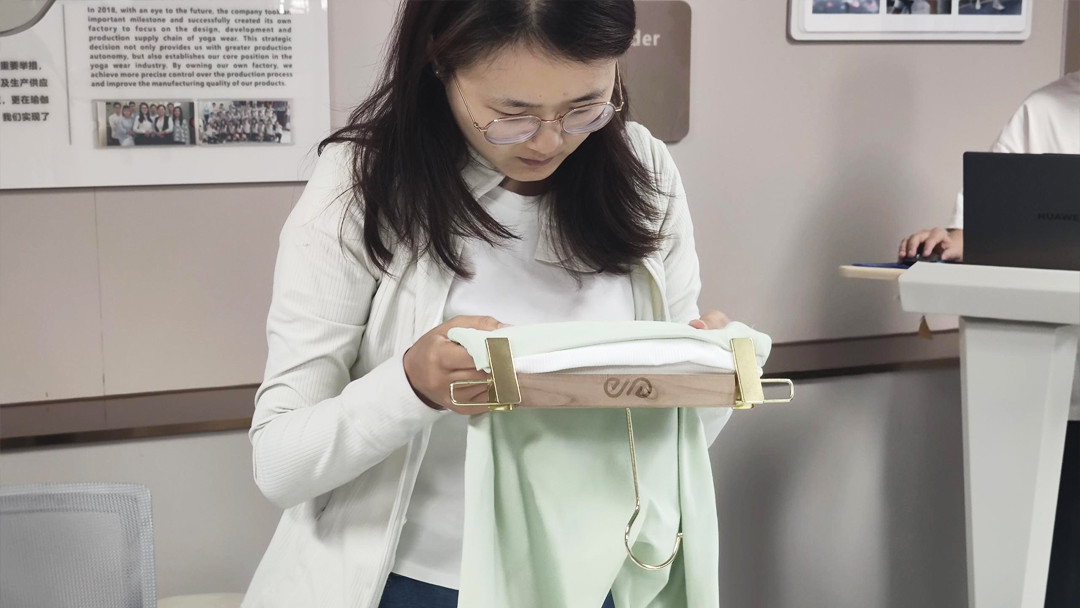 A detailed look at a mint-green activewear garment on a gold hanger being inspected by a quality control designer.