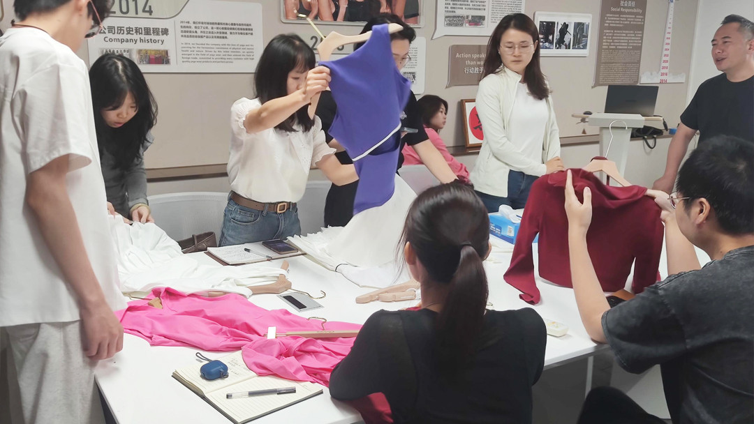 A designer holding up a purple custom sports top for inspection at the manufacturing factory office.