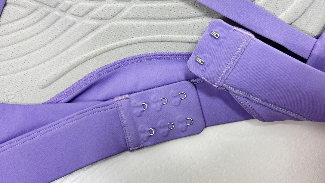 Close-up of a high-impact sports bra's hook-and-eye back closure on a purple garment, showing multi-row adjustment