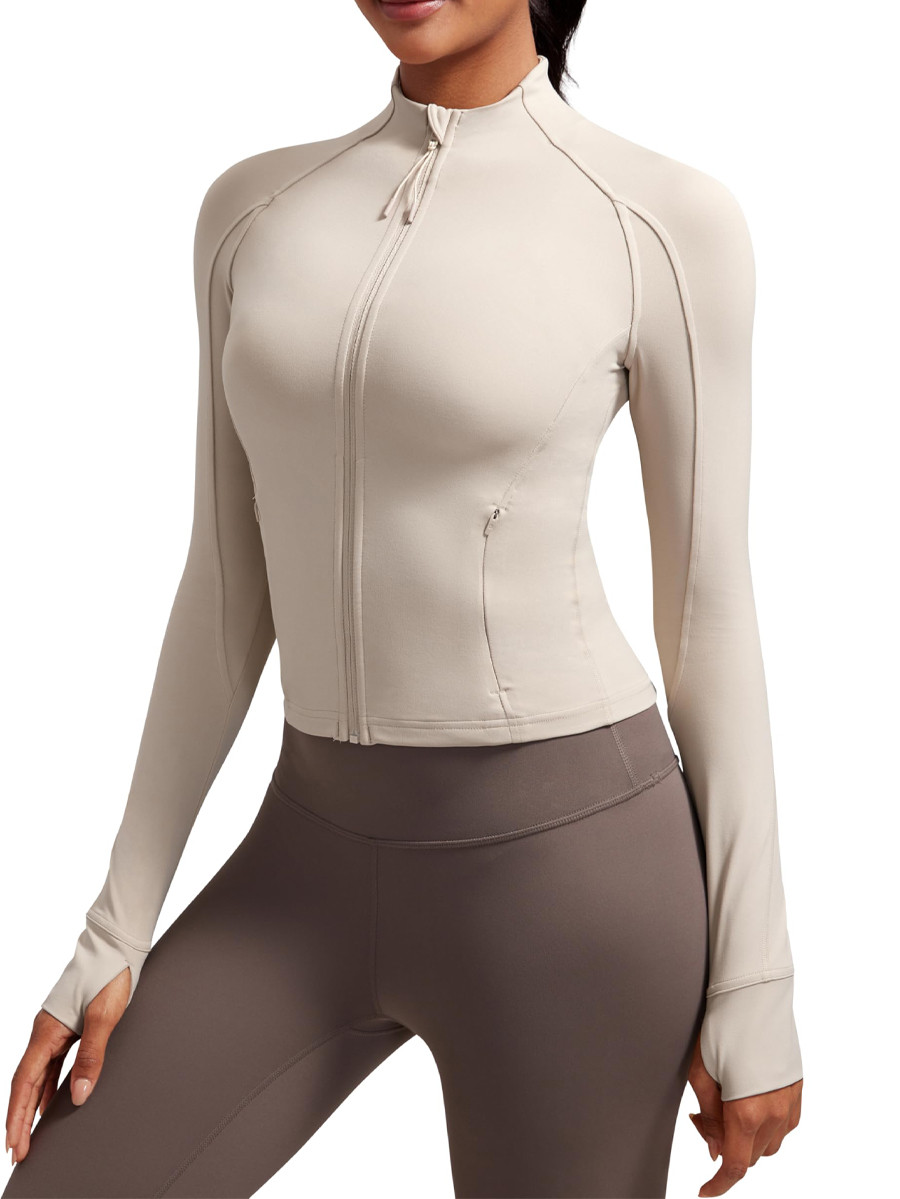 Front view of a women's waist-length slim fit yoga jacket in beige, engineered with buttery soft fabric by a custom activewear manufacturer.