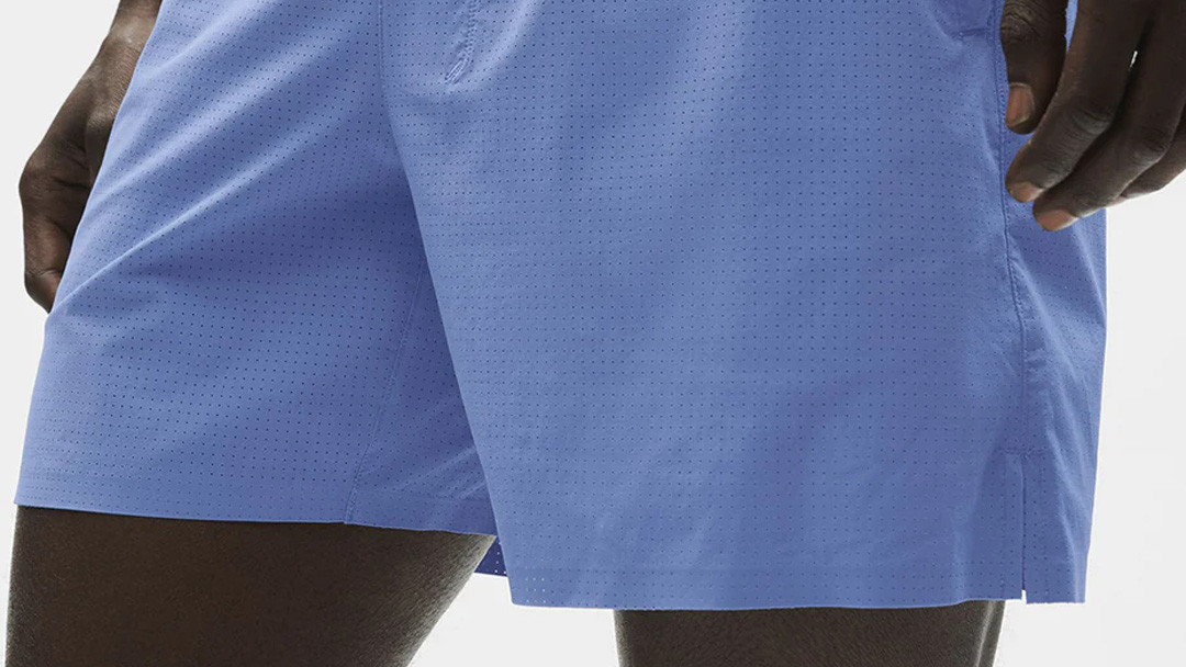 Close-up of men's active shorts showing laser-cut perforation holes on the woven outer shell for ventilation